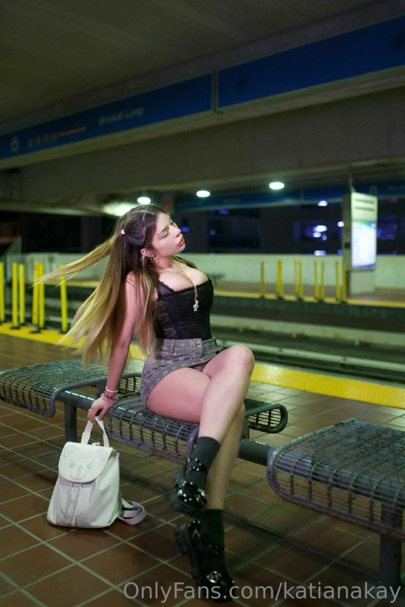 Seductive Katiana Kay sitting on a bench in a black top and short skirt at a train station