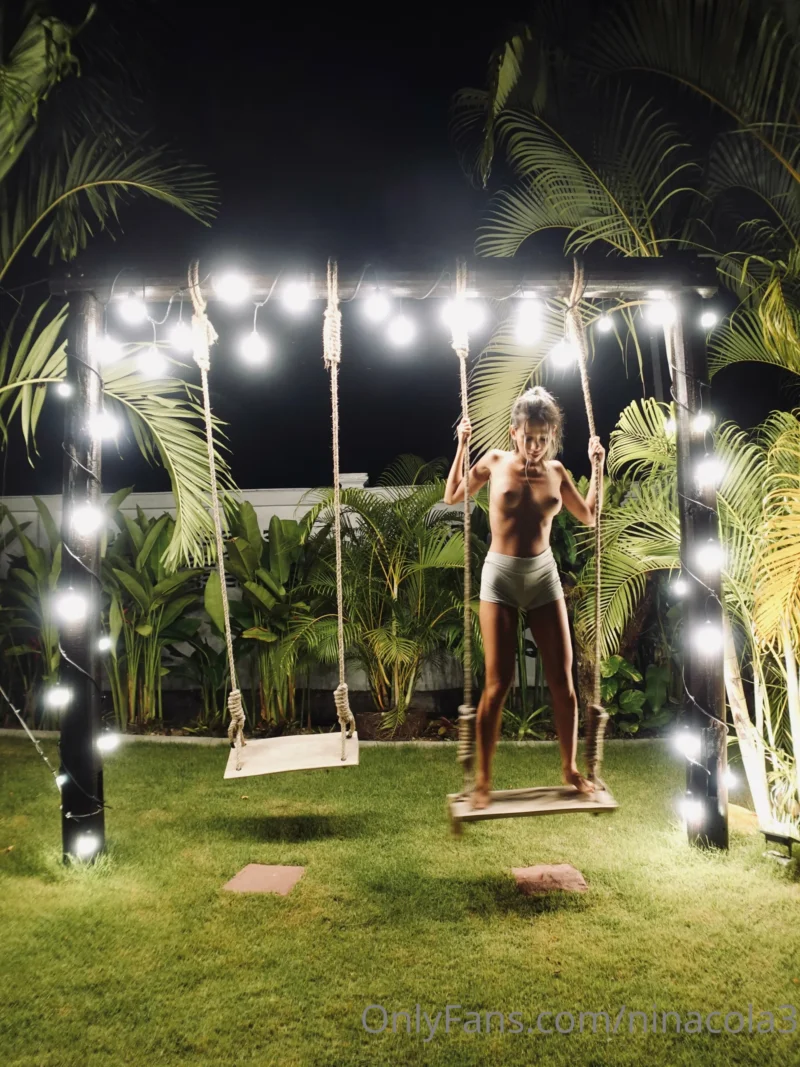 Sexy Nina cola standing on a swing at night, topless in white underwear under string lights