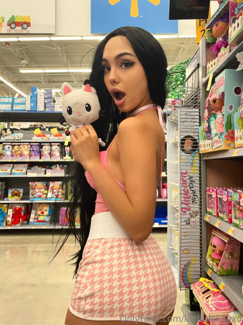 Busty Layla Deline in pink halter top and houndstooth skirt holding plush cat in toy aisle