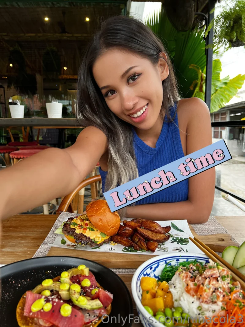 Seductive Nina cola smiling at lunch table with burger and fries in blue top