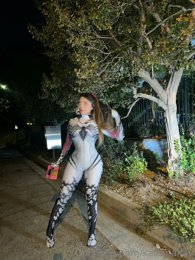 Sultry Katiana Kay in spider-themed bodysuit posing outdoors at night