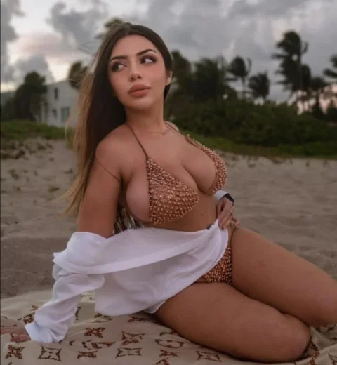 Seductive Katiana Kay kneeling on beach in beaded bikini, white shirt pulled up