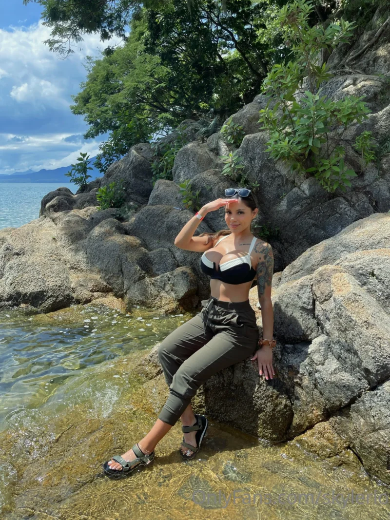 Sexy Skyler Lo in black bra and cargo pants posing on beach rocks by water